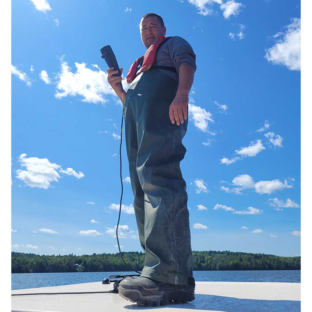 A man holding a temperature probe in front of a lake --- Un homme tenant une sonde de température devant un lac